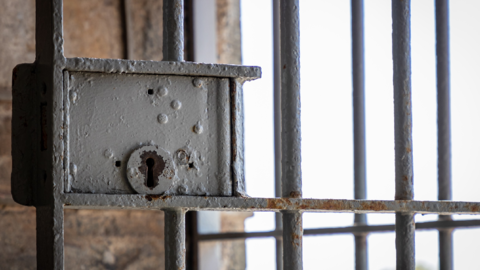 Rusted lock in a prison cell with a view of a grey sky.