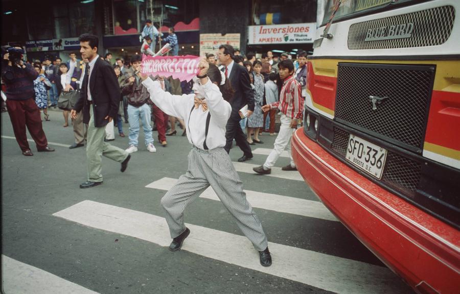 Pedestrians crow an intersection; mime holds paper that reads 
