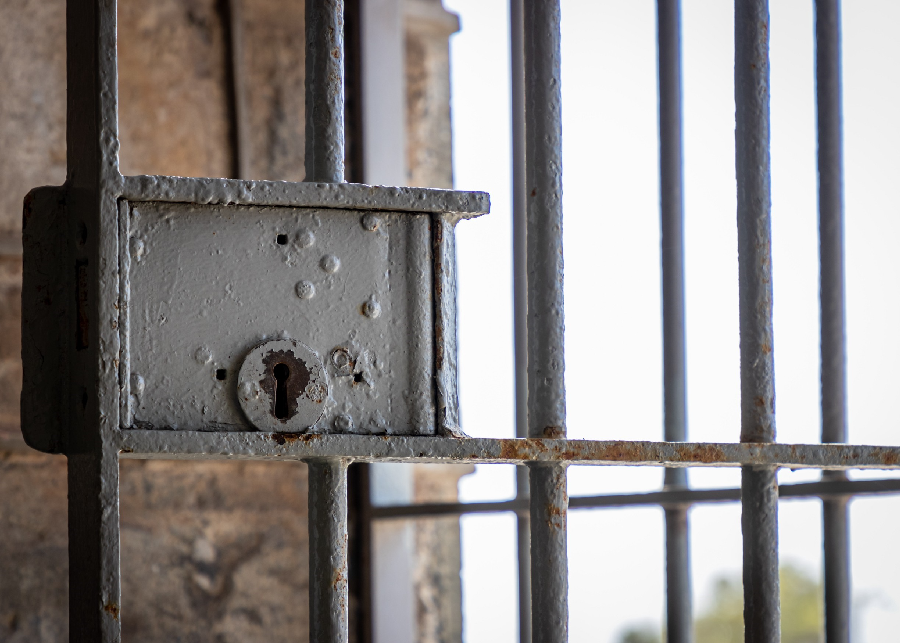Rusted lock in a prison cell with a view of a grey sky.